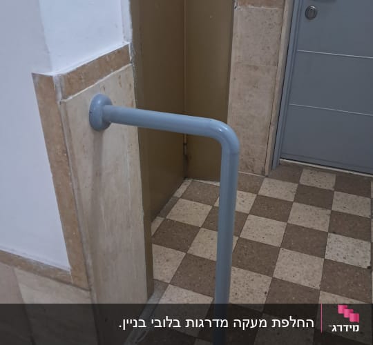 מאחז יד ממתכת אפורה המחובר לקיר ולרצפה במבואת בניין